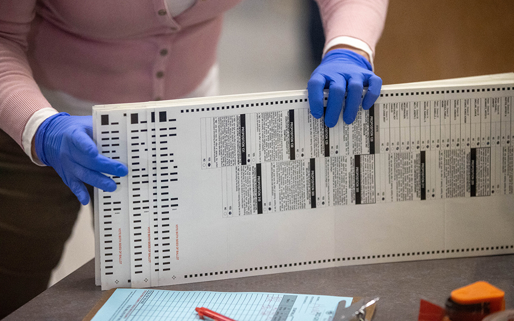 After running through a vote-counting machine, an election worker gathers ballots at the Maricopa County Tabulation and Election Center on Nov. 10, 2022. Maricopa and Mohave counties voted to certify election results Nov. 28, the state deadline, while Cochise County voted to postpone its certification. (File photo by Drake Presto/Cronkite News)