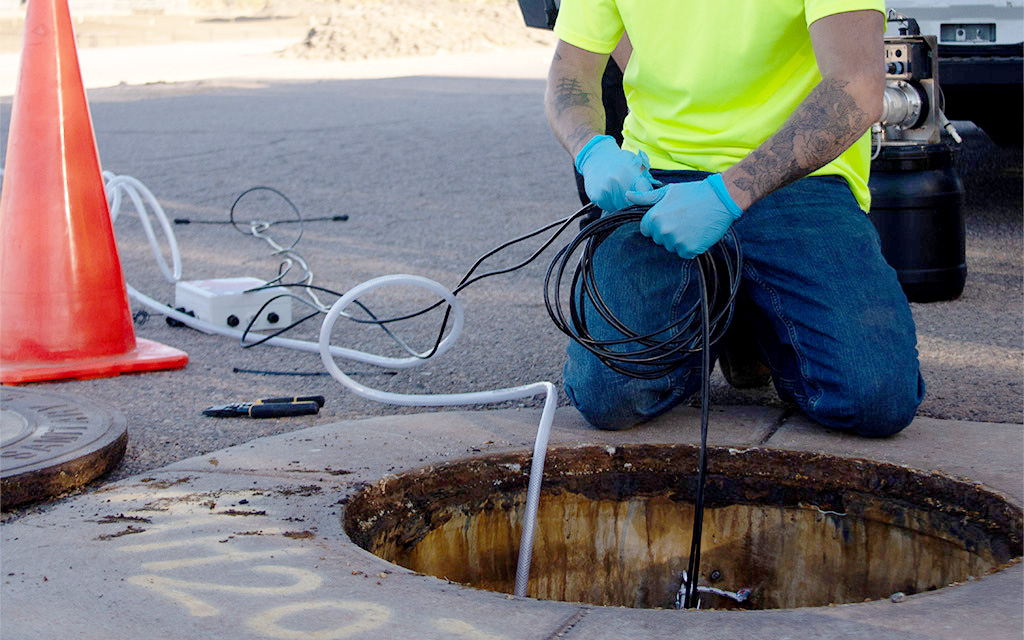 An employee of RDH Environmental Services installs a Kando Pulse device inside a sewer system near Broadway Road and 83rd Avenue in Phoenix on Nov. 8, 2023. (Photo by Ellie Willard/Cronkite News)