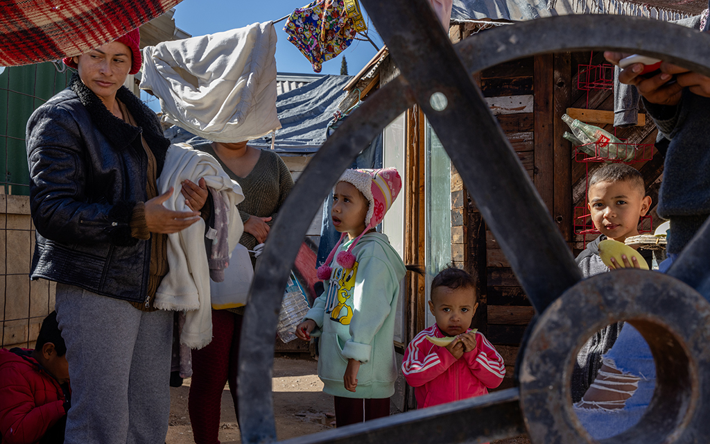 A family of migrants, including, from left, Ruth Barrera, 32; Arlene Carmona, 7; Luis David Araujo, 7; and Marta Araujo, 2, eats fruit and does laundry on Feb.12, 2024, outside their temporary home in Nogales, Sonora, Mexico, as they await their asylum court date in the U.S. (Photo by Kayla Jackson/Cronkite News)