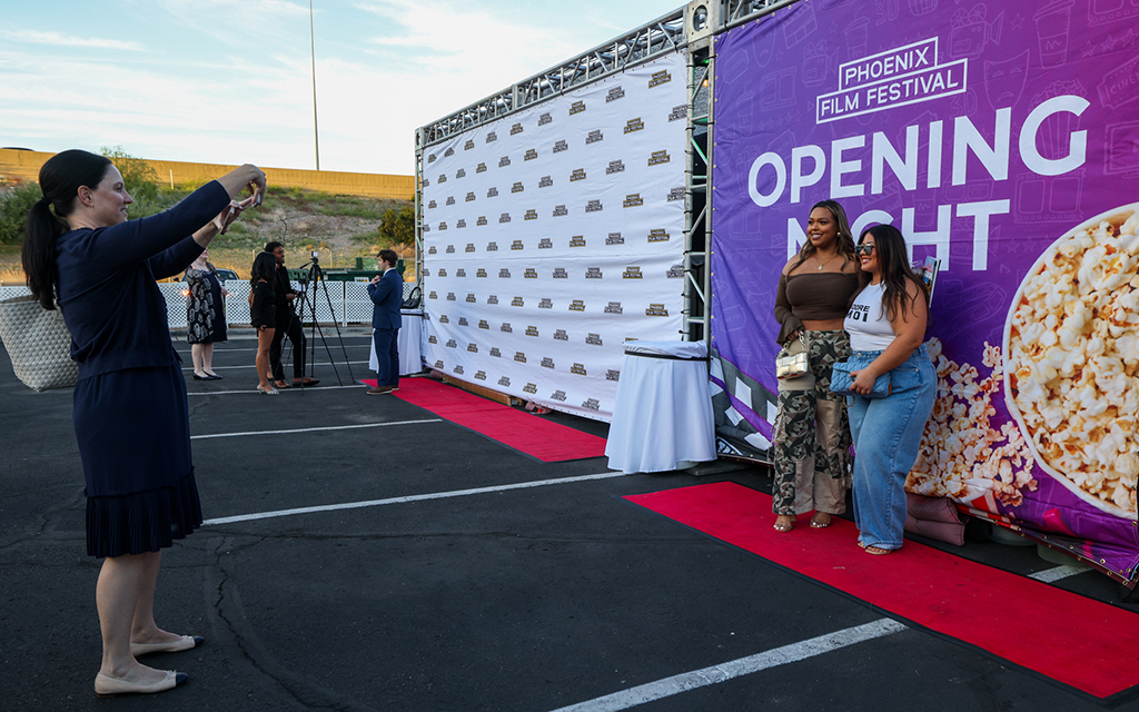 Nicole Simone and Karen Genis get their photo taken in front of the “Opening Night” banner at the Phoenix Film Festival’s kickoff event at the party pavilion next to the Harkins Theatres: Scottsdale 101 on April 4, 2024. Simone and Genis were at the film festival for the first time. (Photo by Kayla Mae Jackson/Cronkite News)