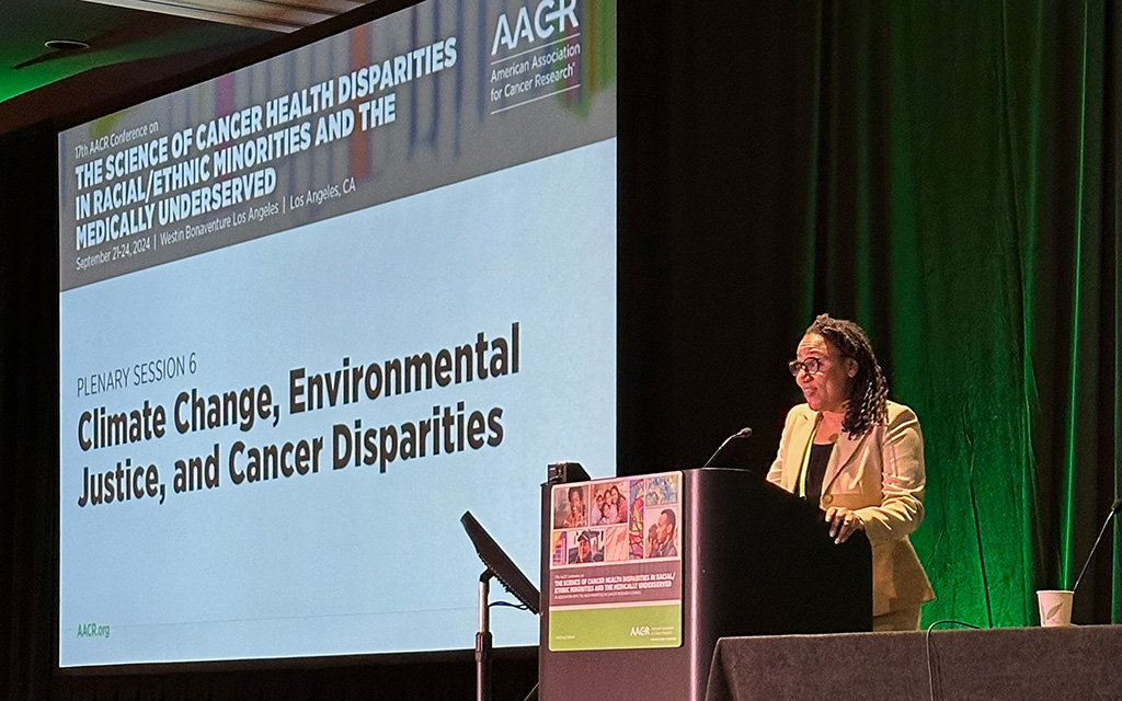 Speaker at a lectern with a projection screen displaying conference information at the 17th AACR Conference.