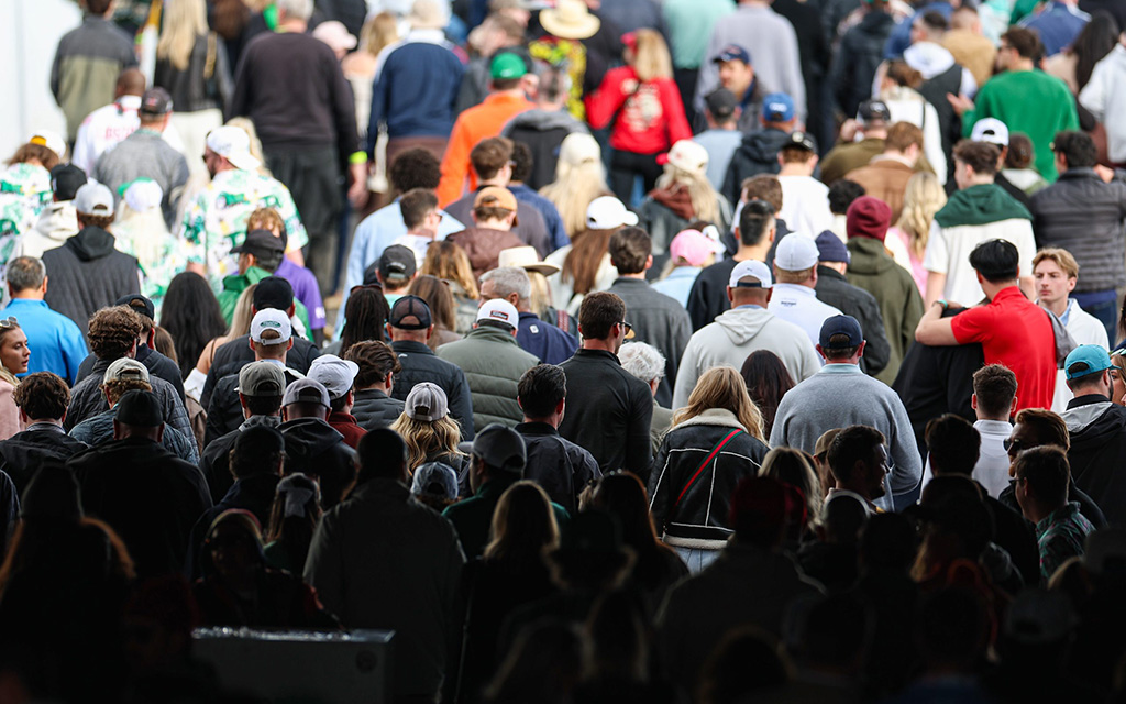 A large crowd of people walking away in a densely packed corridor, wearing casual clothing.