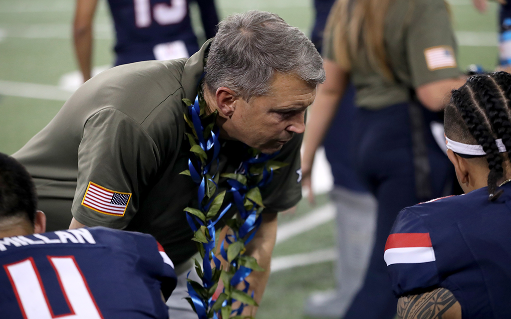 Brent Brennan with a lei around his neck talking to two Arizona football players on the sideline.