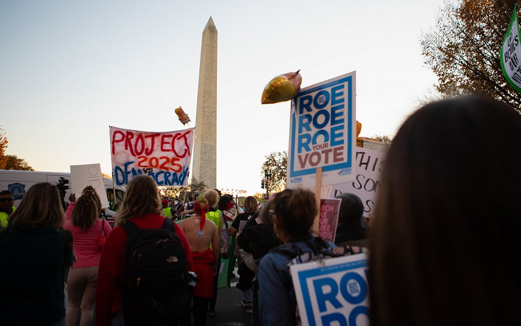 Demonstration near the Washington Monument with people holding signs, including “ROE ROE ROE YOUR VOTE” and “PROJECT 2025.”