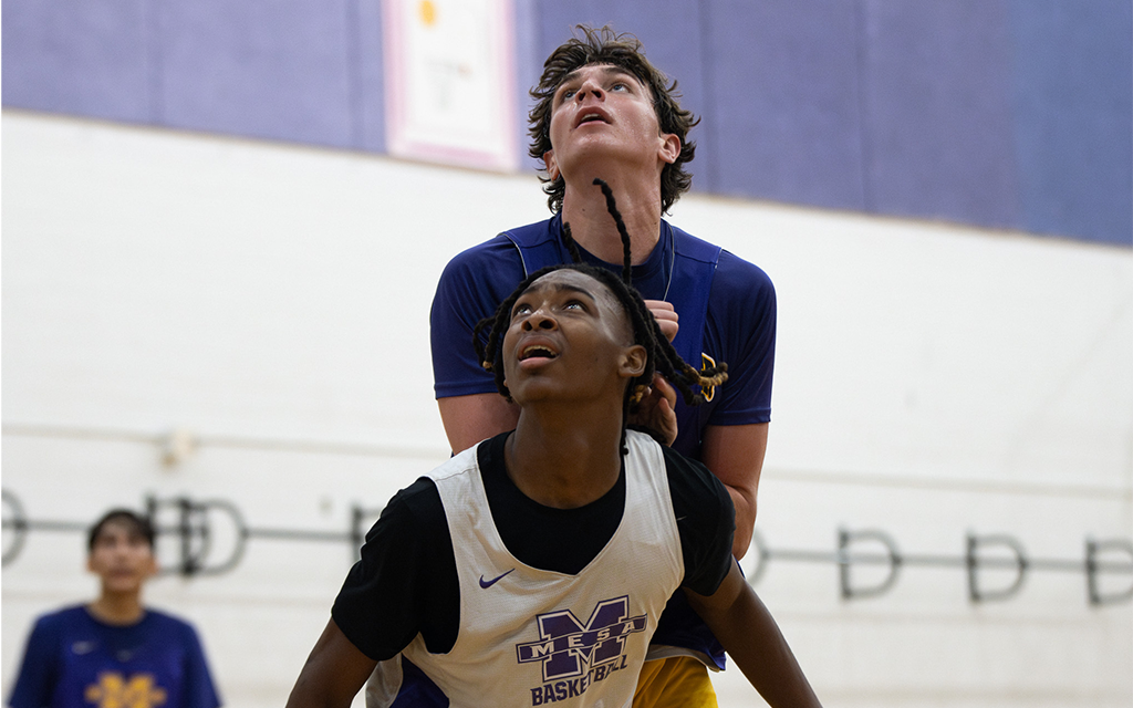 Two basketball players look above awaiting to rebound a basketball