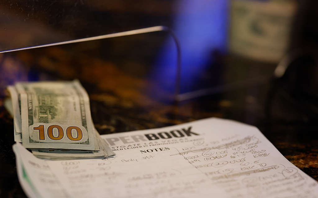 Stack of US 100-dollar bills on a marbled counter with a paper titled "SUPERBOOK" underneath.
