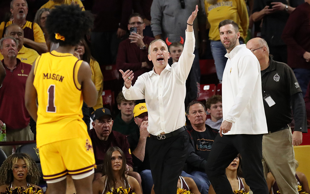Basketball game scene with Arizona State Basketball player Alston Mason, ASU head coach Bobby Hurley, and spectators in the background.
