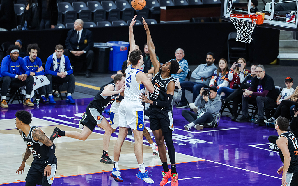 Two basketball players jump to reach the ball on a purple court during a game.