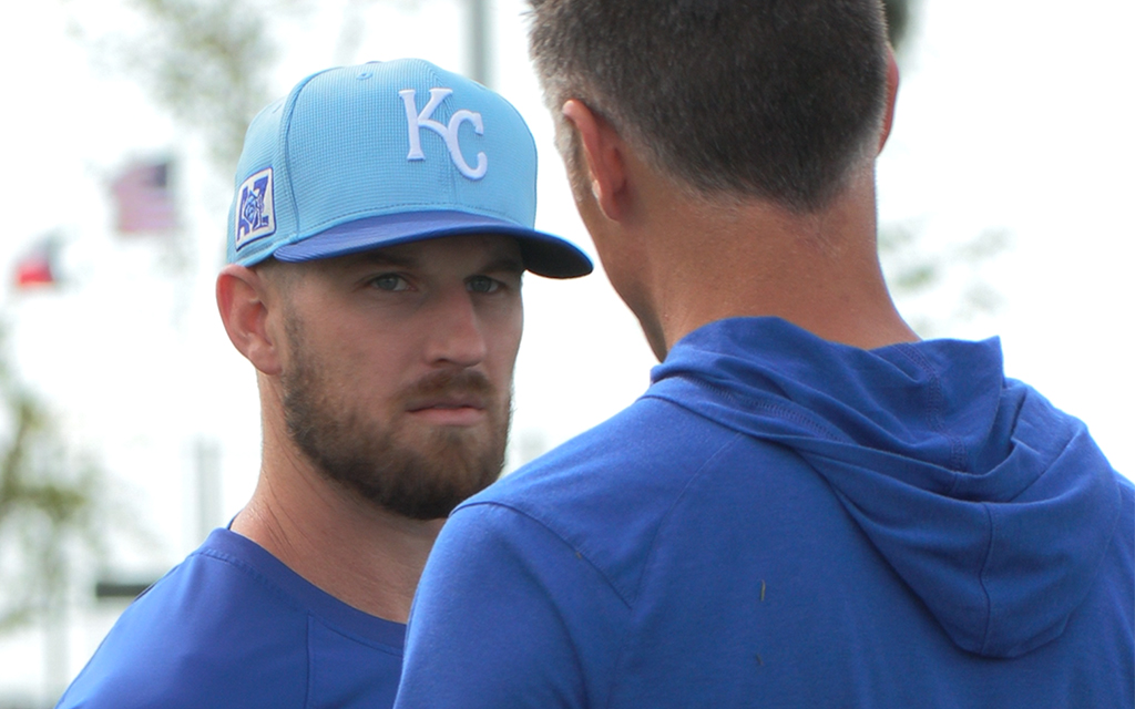 Two people wearing blue shirts, one with a "KC" cap, outdoors.