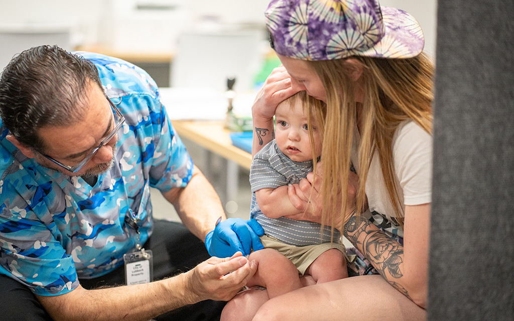 A health professional gives a vaccine to a child sitting on a woman's lap.