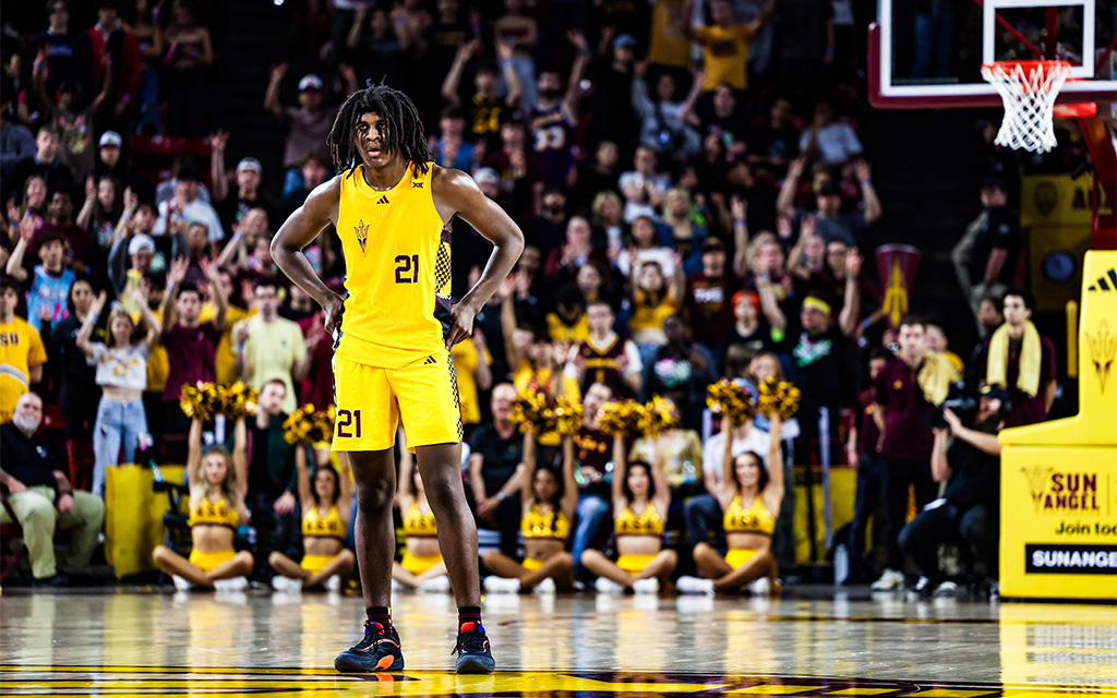 Basketball player in a yellow uniform stands on the court surrounded by cheering fans and cheerleaders.