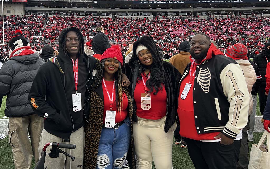 The Tyson family pose together on a football field with a crowd in the background.