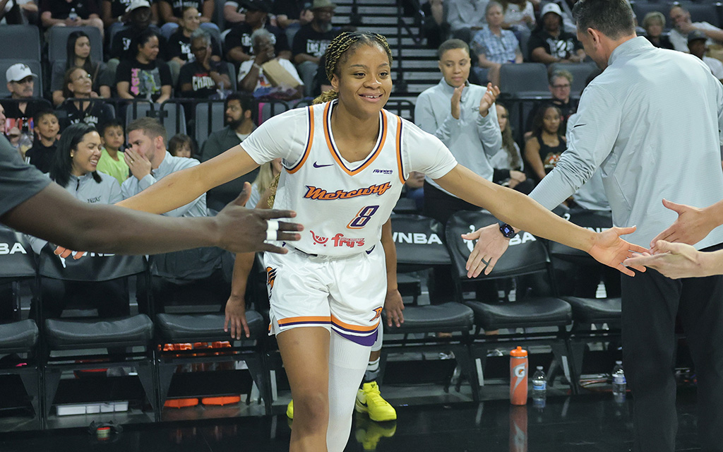Monique Akoa Makani in a white uniform high-fiving her teammates as she enters the court.