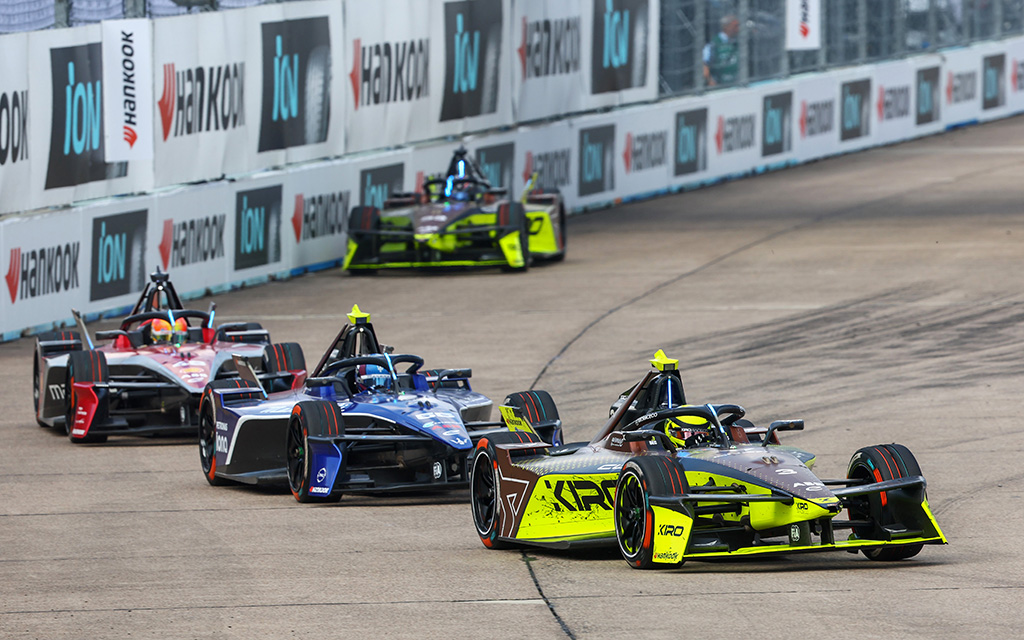 Four Formula E cars racing on a curving track with advertising banners in the background.